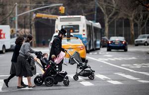 Een joodse man en twee vrouwen duwen kinderwagens voor zich uit terwijl ze een straat oversteken in de Joodse wijk van Brooklyn in New York City. De burgemeester van New York heeft een vaccinatieplicht afgekondigd. beeld AFP, Johannes Eisele