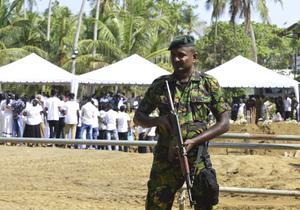 Terwijl achter hem de begrafenis plaats vindt van een slachtoffer van de bomaanslagen, houdt in de stad Negombo een Srilankaanse militair de wacht.  beeld AFP, Lakruwan Wanniarachchi​