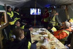 ‘Gele hesjes’ kijken maandagavond in Montabon, tussen Le Mans en Tours, naar de toespraak van president Macron. beeld AFP, Jean-Francois Monier