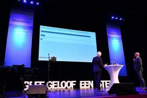 De CU-bestuursleden Piet Adema (l.) en Klaas Tigelaar (r.) volgen de stemmingen over de door de leden ingediende moties en amendementen vanaf het podium. beeld ANP, Eric Brinkhorst