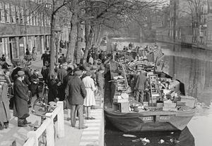 Aan de Lijnbaansgracht in Amsterdam worden dekschuiten volgeladen met huisraad uit ontruimde huizen van weggevoerde Joodse inwoners. Omstanders tonen grote belangstelling voor de spullen. beeld uit "De Jodenvervolging in foto’s"