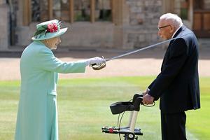 De Britse koningin Elizabeth slaat Tom Moore tot ridder. beeld AFP
