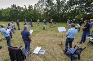 Mannenensemble Lezzom uit het Zeeuwse Gapinge repeteert sinds 1 juni –als het weer het toelaat– wekelijks in de buitenlucht. Normaal oefenen de zestien mannen in een dorpshuis, maar binnen zingen vinden ze nu te gevaarlijk omdat de meeste koorleden tot een risicogroep behoren. Koorlid Huib Lievense: „Het was eerst wennen, omdat we op redelijke afstand van elkaar staan. Maar het gaat steeds beter en het is ook fijn dat we elkaar zien én met elkaar kunnen praten.” beeld Dirk-Jan Gjeltema