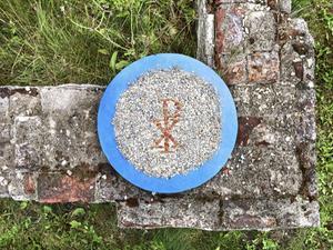 Het zogeheten Christusmonogram bevat de eerste twee Griekse letters van de naam van Christus, chi en rho. Voor de serie ”Kerk in 2050” vormde fotograaf Sjaak Verboom mozaïeken van oude christelijke symbolen, gemaakt van de rode steen van de in 2015 afgebroken kerk van Garsthuizen. Een deel van de stenen van de Groningse kerk is bewaard gebleven, in de hoop dat het bedehuis ooit kon worden herbouwd. De mozaïeken zijn gefotografeerd op de fundamenten van de kerk, die nog altijd zichtbaar in het landschap liggen. Zo ontstaat er perspectief vanuit een gebroken kerk: in verbondenheid met het verleden is er verwachting voor de toekomst. beeld Sjaak Verboom