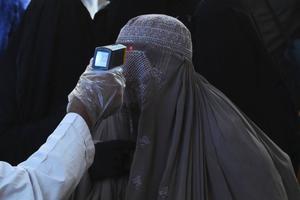 Een gezondheidsfunctionaris controleert de lichaamstemperatuur van een in een boerka geklede vrouw. beeld AFP, Arif Ali